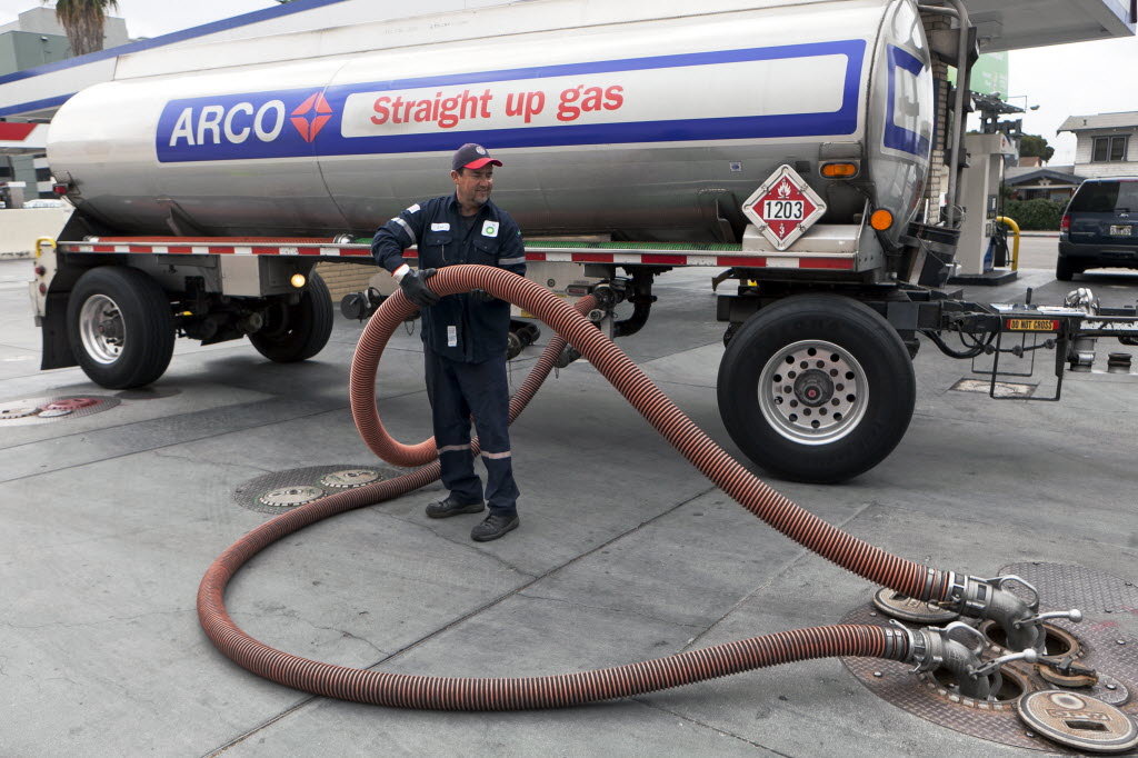 A man connects hoses from a gasoline delivery truck to an in-ground tank