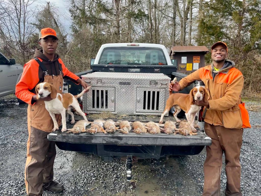 Two hunters in safety orange pose with their dogs and their harvest