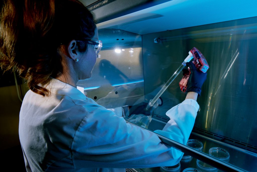 A woman in a lab conducts a test by injecting something into a beaker.