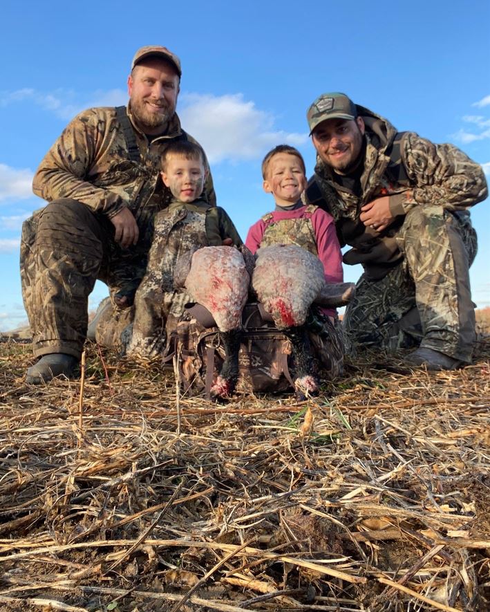 Two men and two children pose in a field with several geese they have shot.
