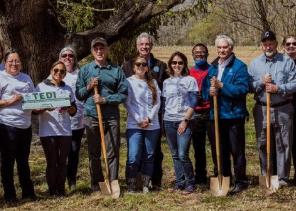 A group of officials and citizens pose with shovels during a tree-planting event.